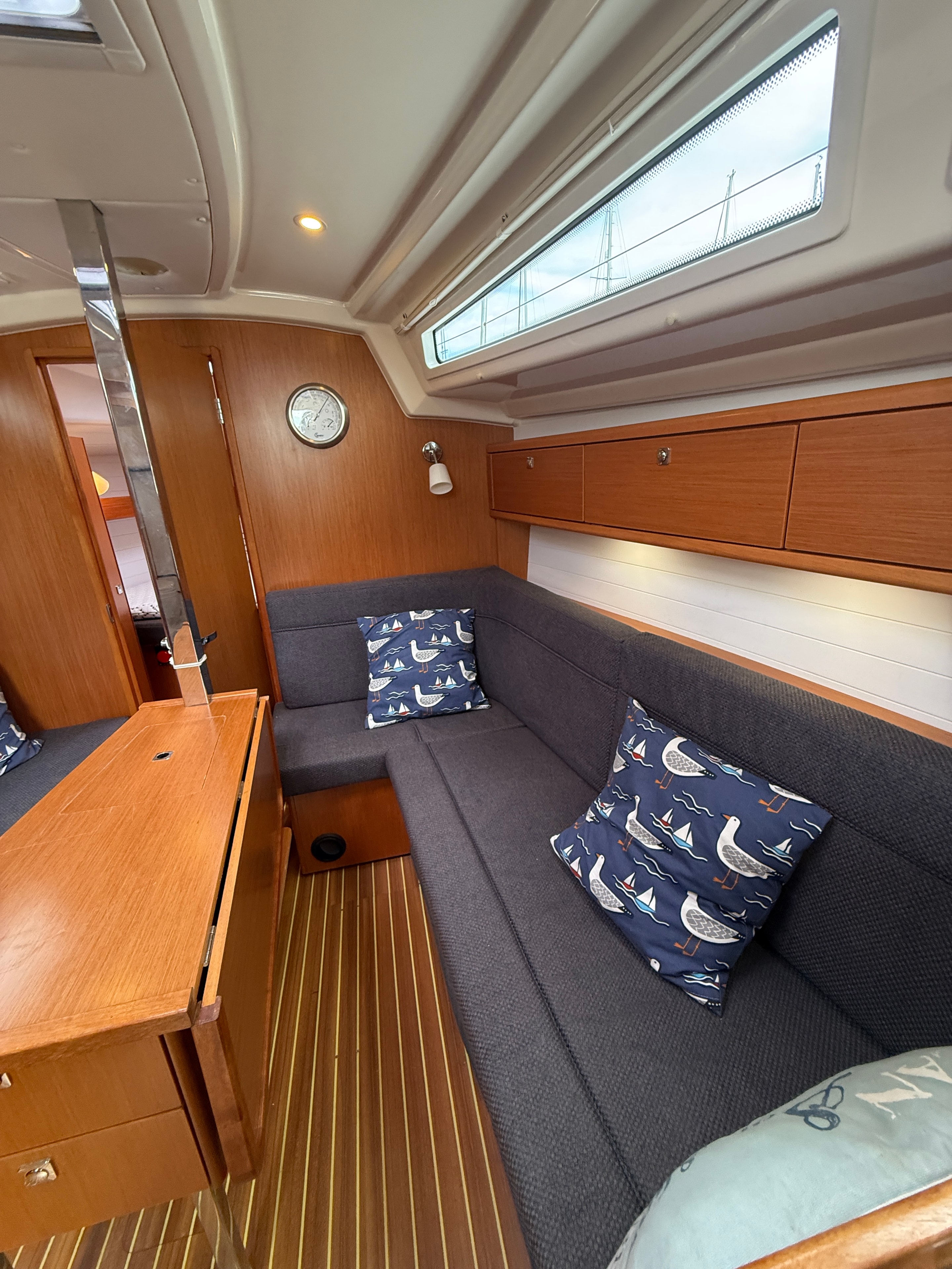Saloon — grey settee, nautical cushions, teak table, barometer